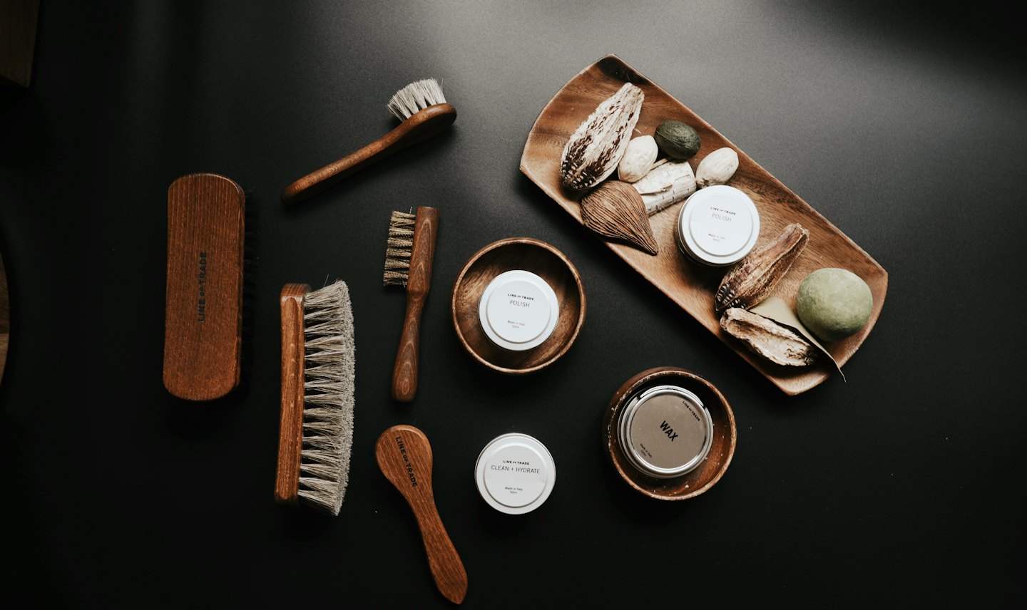 Shoe care products and dried botanicals on a dark surface.